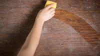 a hand cleaning dust off a wooden surface with a yellow sponge